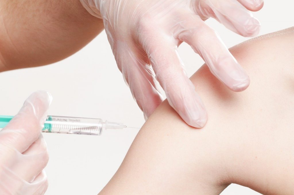 A person with a medical glove on giving a vaccine into a shoulder.