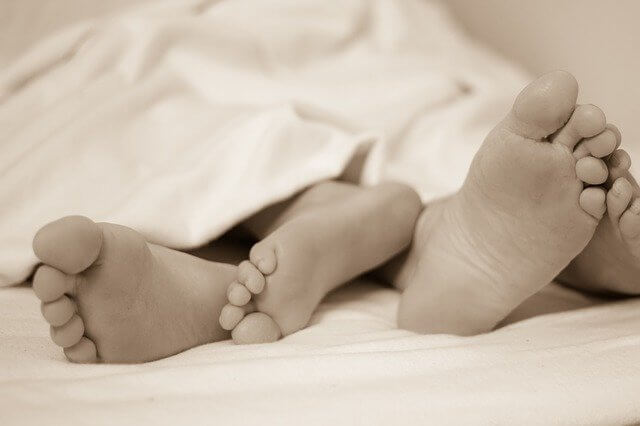 A man and woman in bed, with feet sticking out of the duvet.